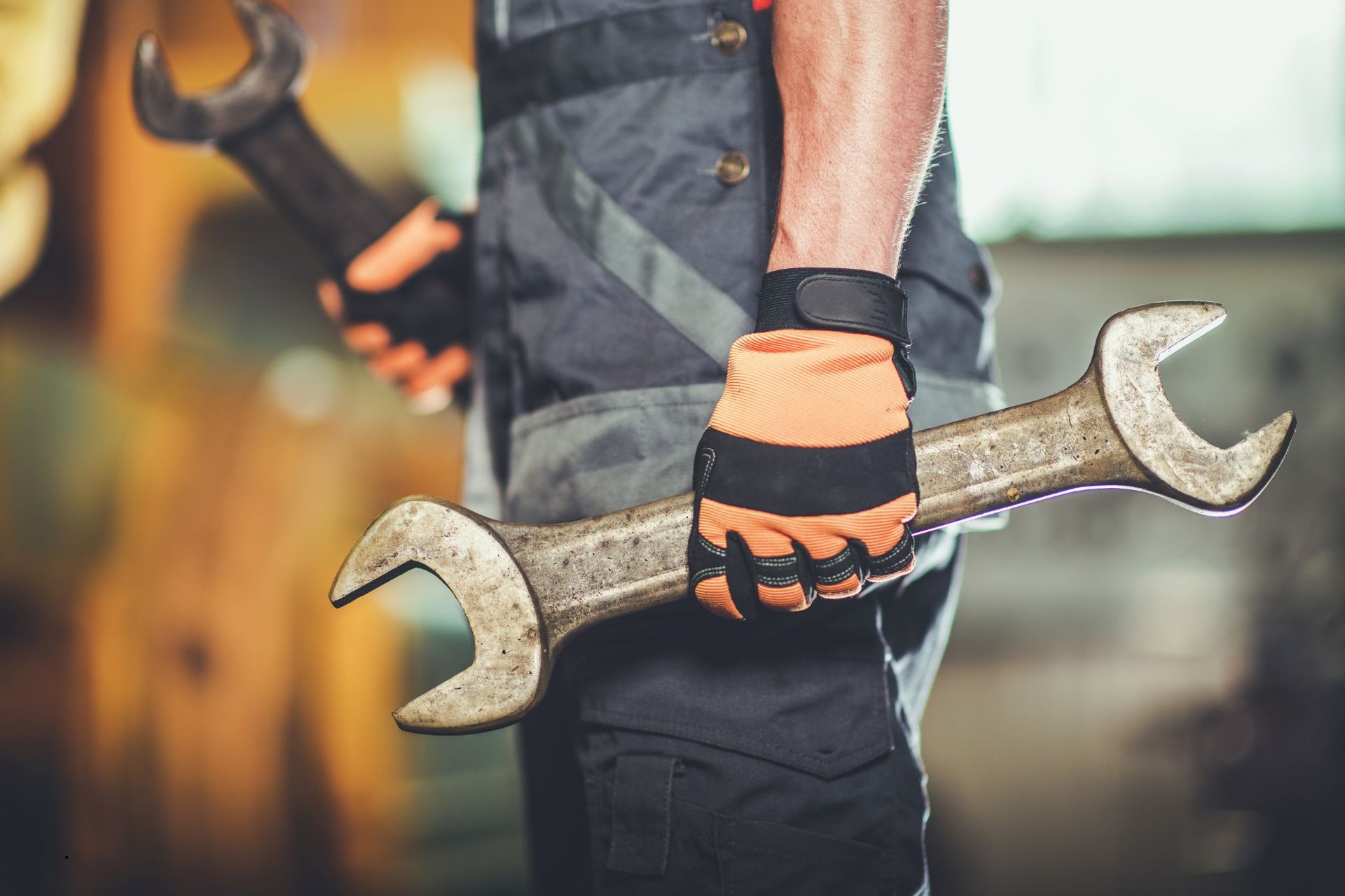 Technician in orange work gloves carrying two large open-end wrenches through the shop