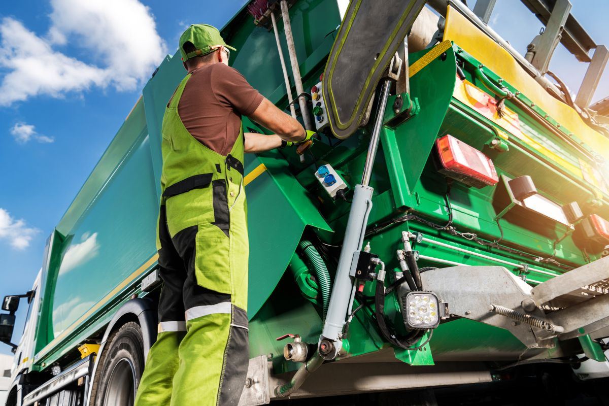 Sanitation worker operating controls on a green refuse collection truck