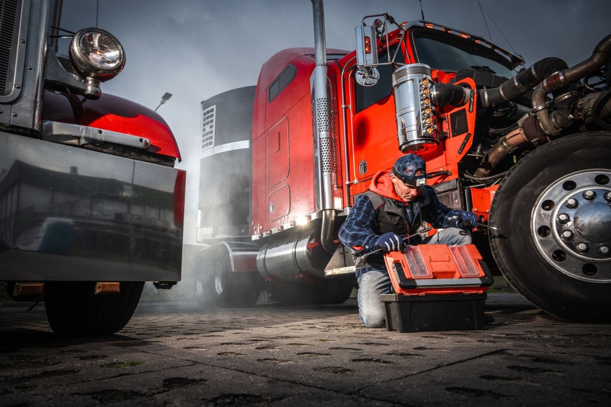 Technician working underneath a red semi truck in a service bay